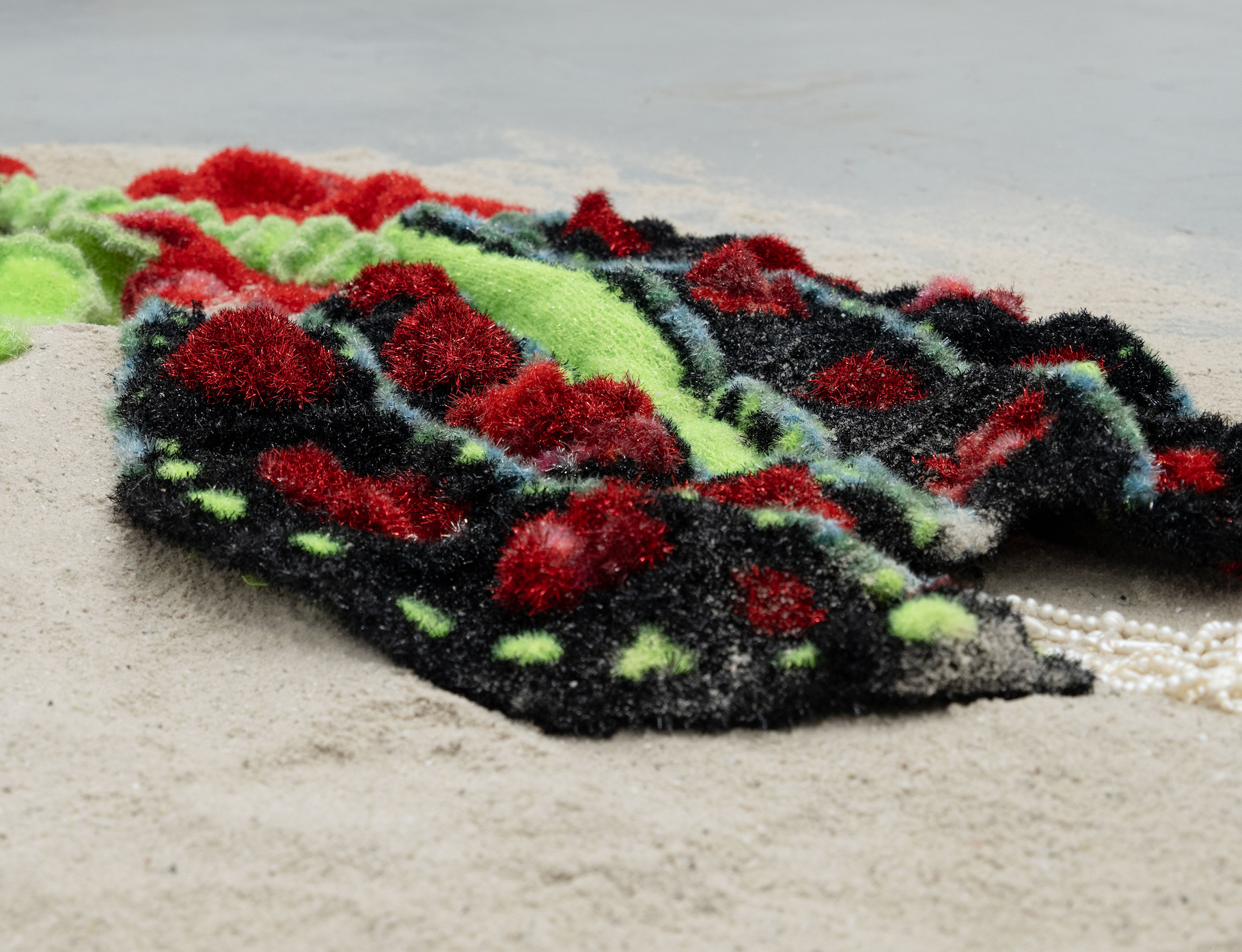 Close view of red, black and green polyester yarn on sand