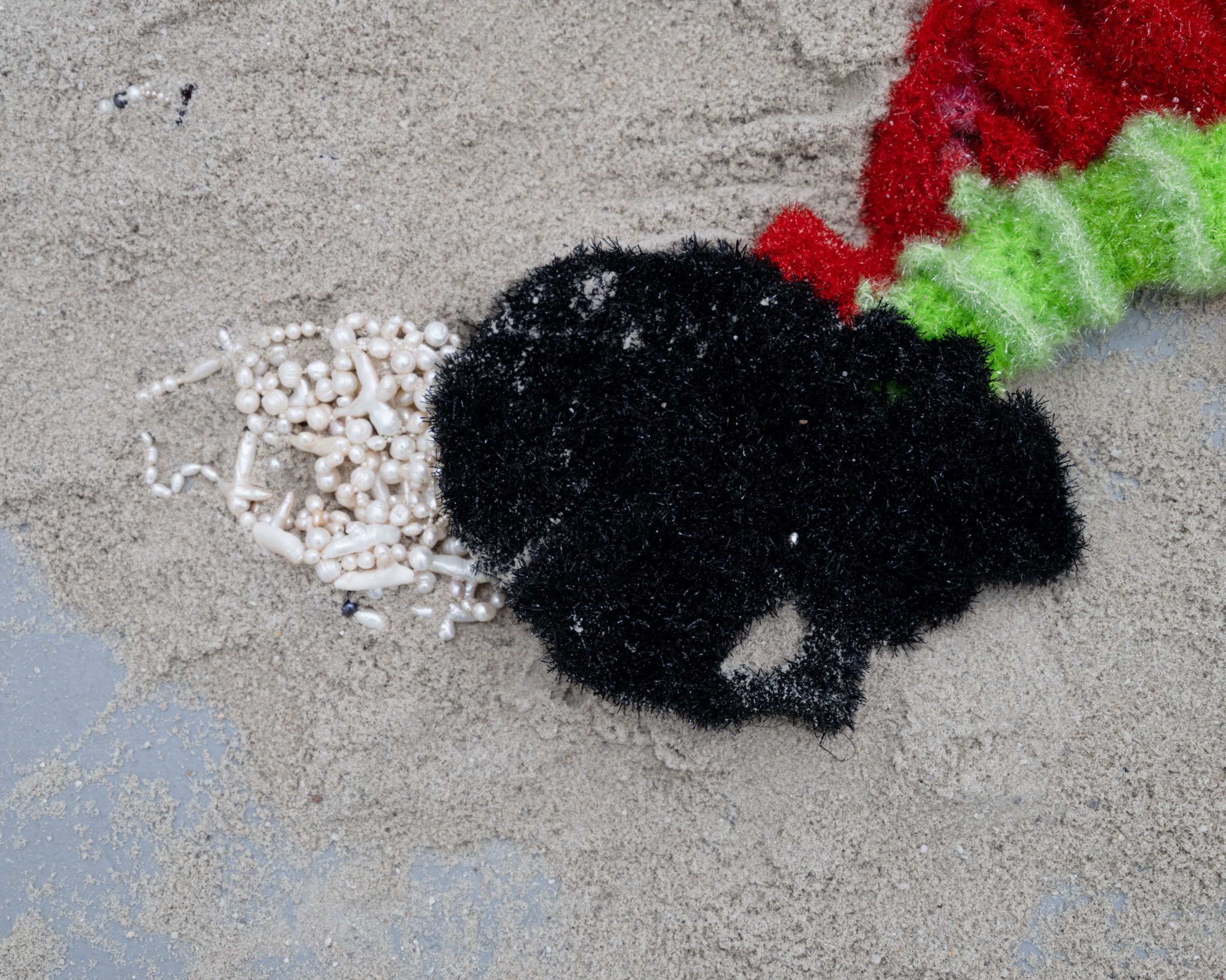 Black polyester yarn form beside scattered pearls
